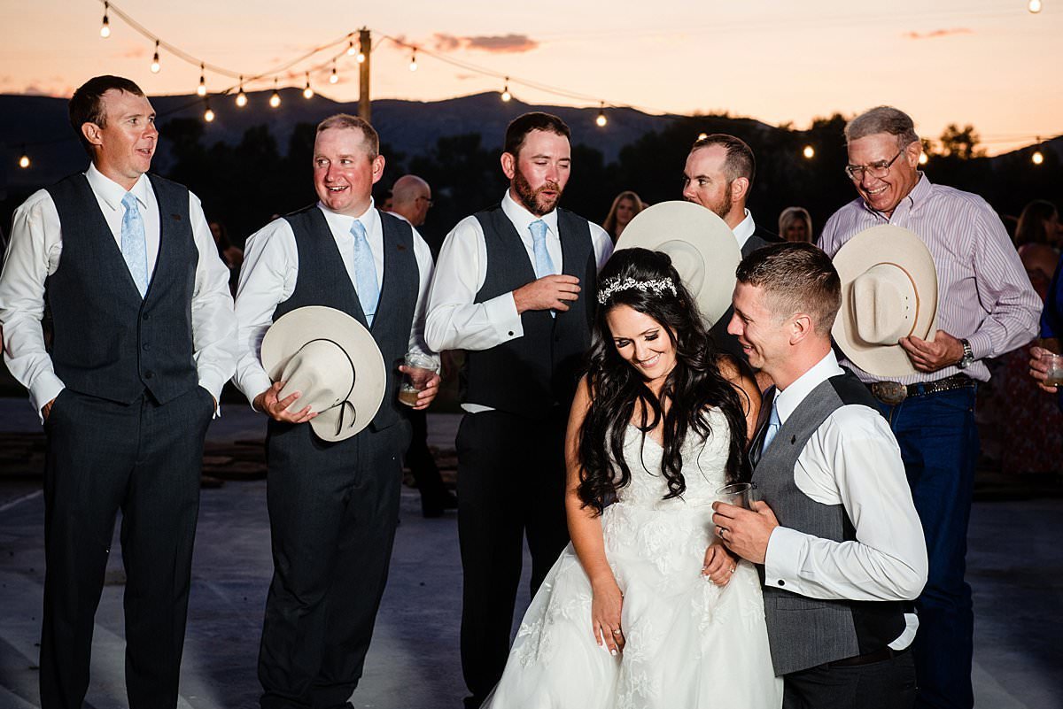 Close up photo of bride sitting on her husbands knee while his fraternity brothers sing to them