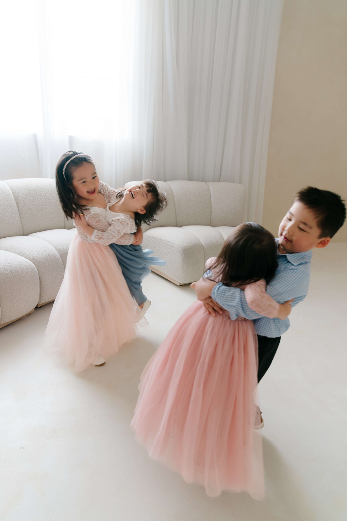 Two pairs of siblings spin and laugh, dressed in pastel gowns and shirts during a family photo session.