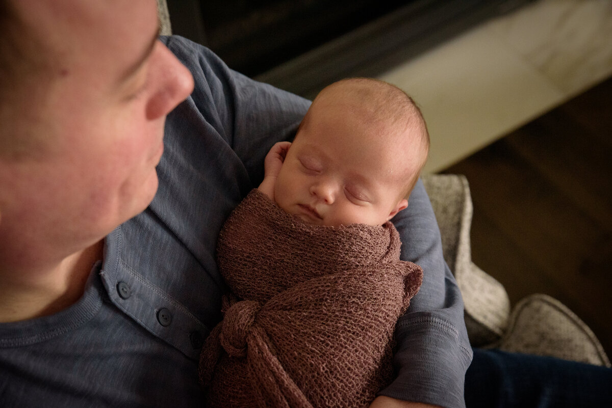 Dad is holding newborn daughter who is wearing a dusty rose wrap in their home in Green Bay, Wisconsin.