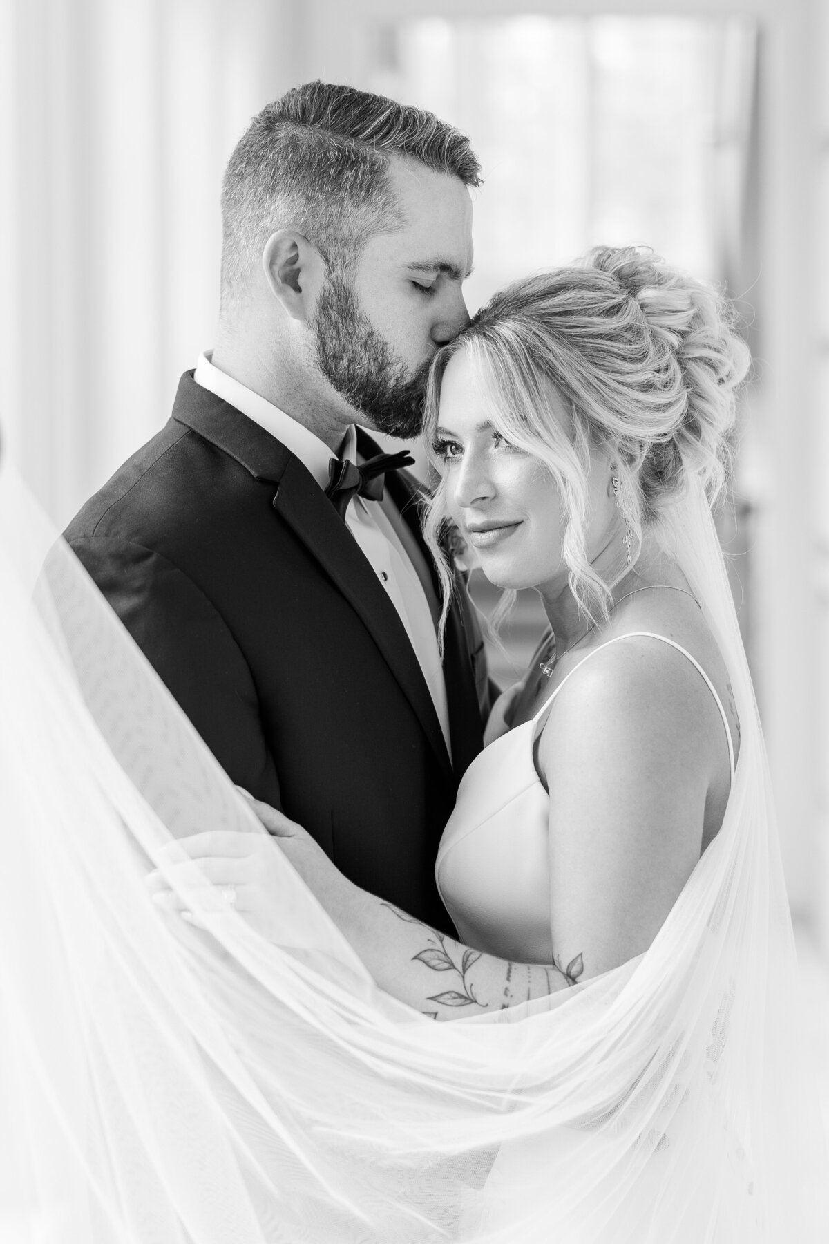 black-and-white-image-of-groom-kissing-brides-forehead-with-swooping-veil
