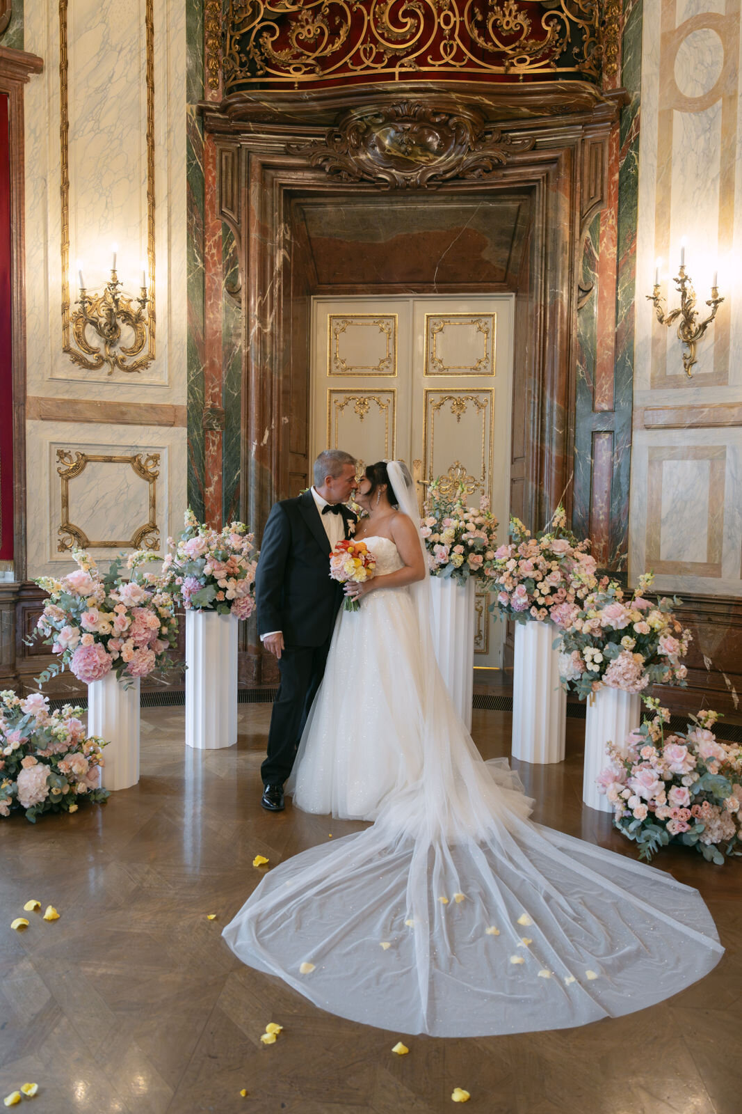 Newlyweds kissing at the wedding ceremony surrounded by flower arrangements at palace Daun Kinsky in Vienna