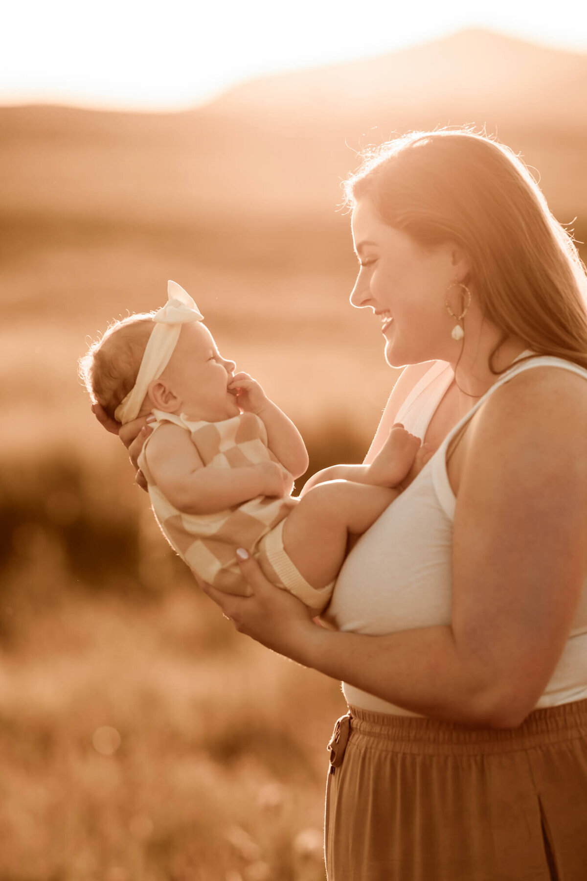 Mother looks at her smiling baby with the sunset in the background, OKC family photography.