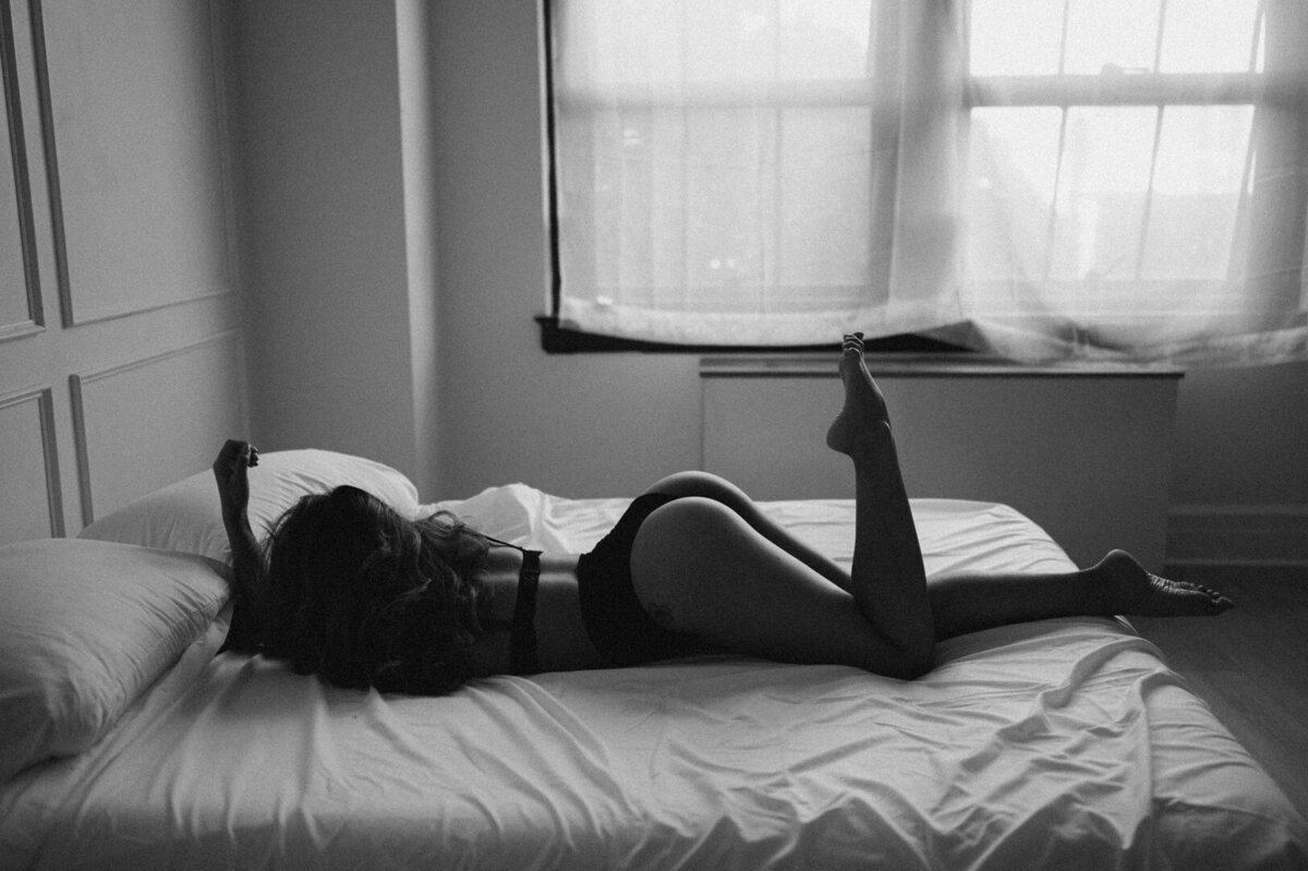 Brunette woman laying on a white bed wearing black lingerie taken by Kayleen Lim a Washington boudoir photographer