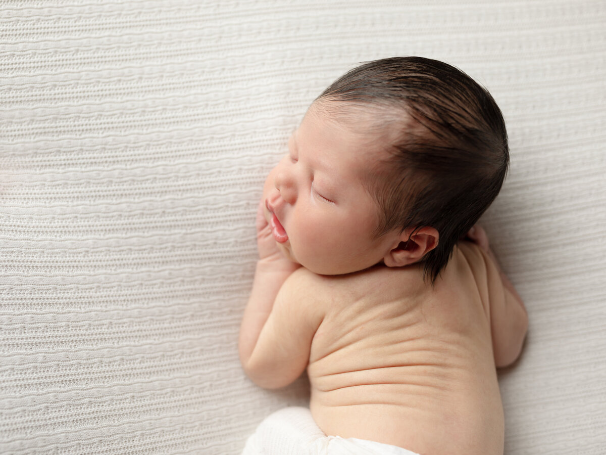 newborn baby boy in white pants posed for newborn photography