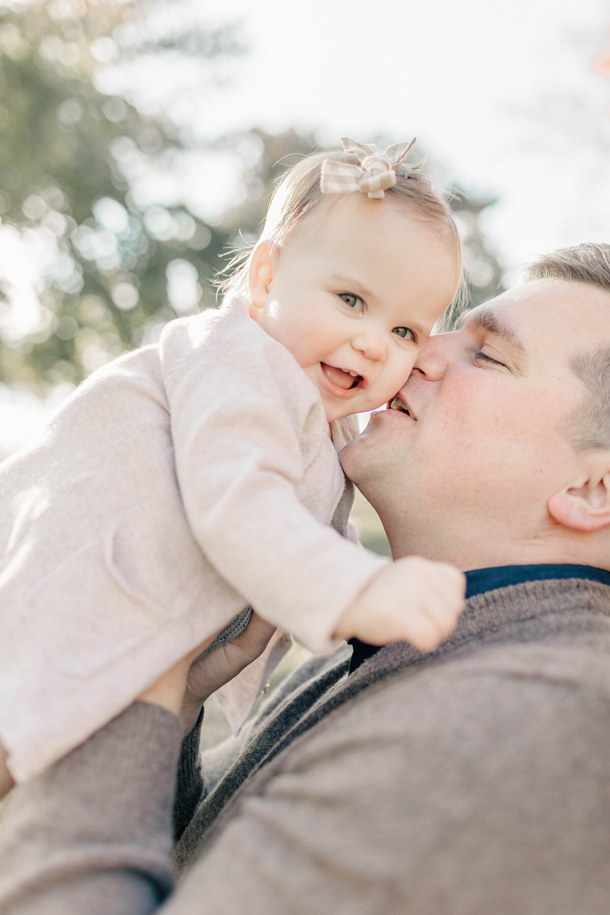 Father kissing his baby girl’s cheek while she smiles during her Kansas City one-year milestone session.