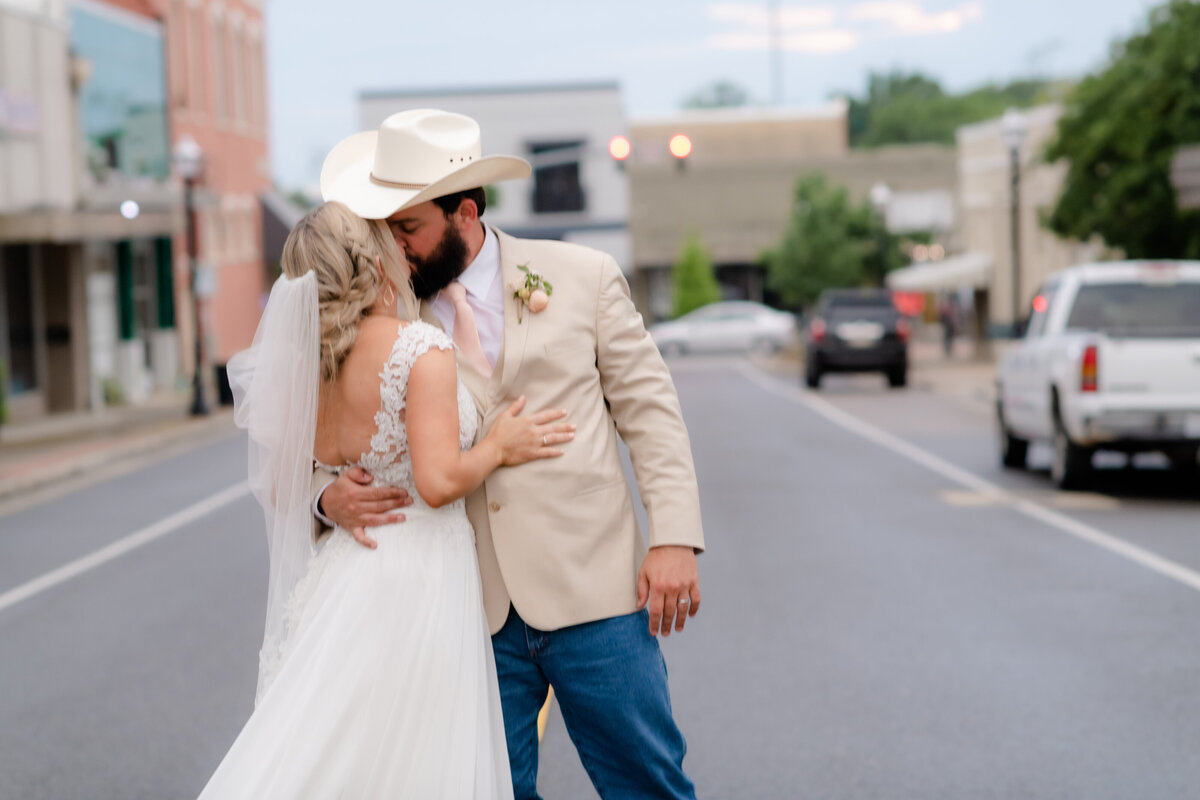 groom brings his bride to him by grasping at her waist and kissing her in the middle of downtown