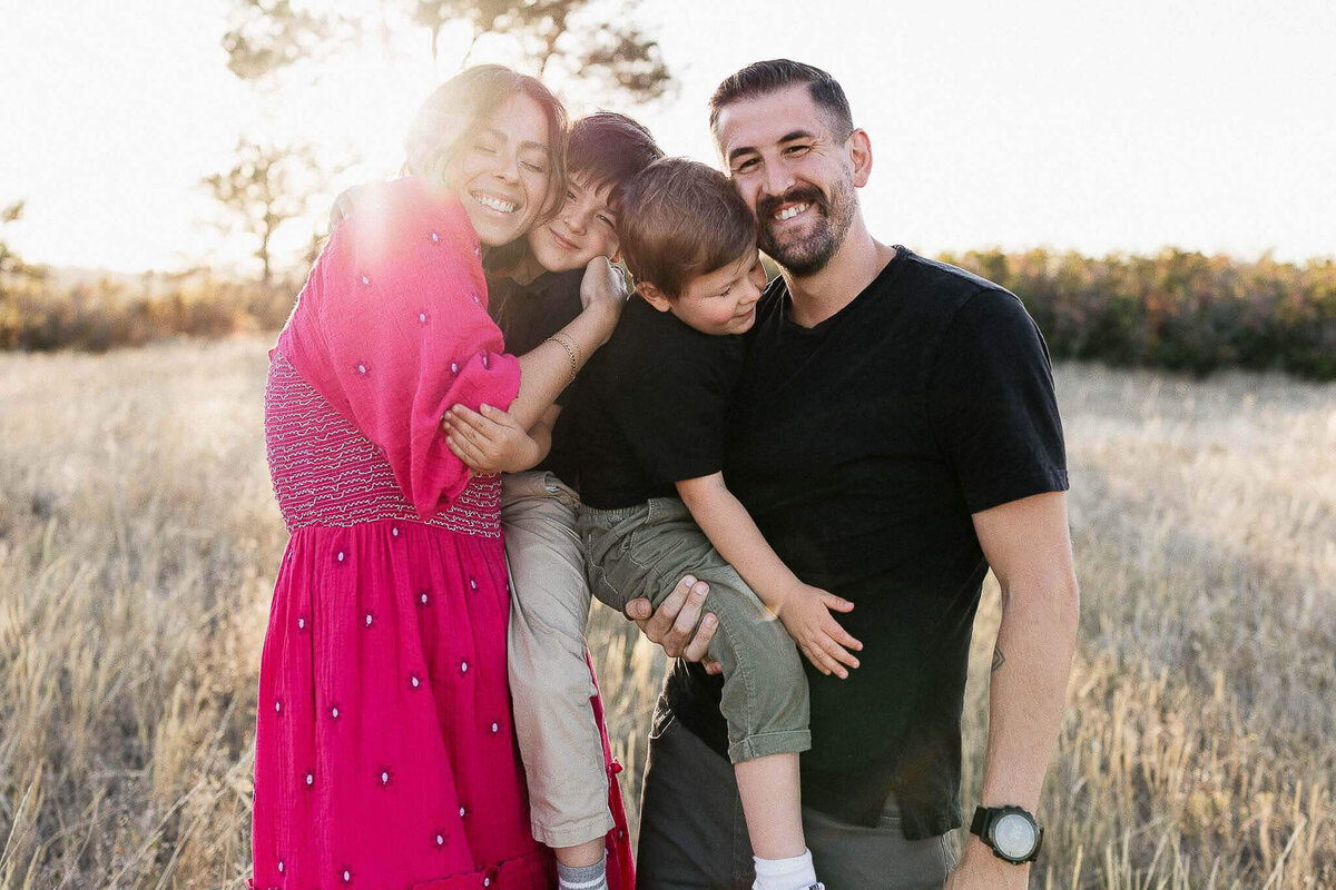 Family of four embracing in field during fall. Cleveland family photographer capturing authentic moments.
