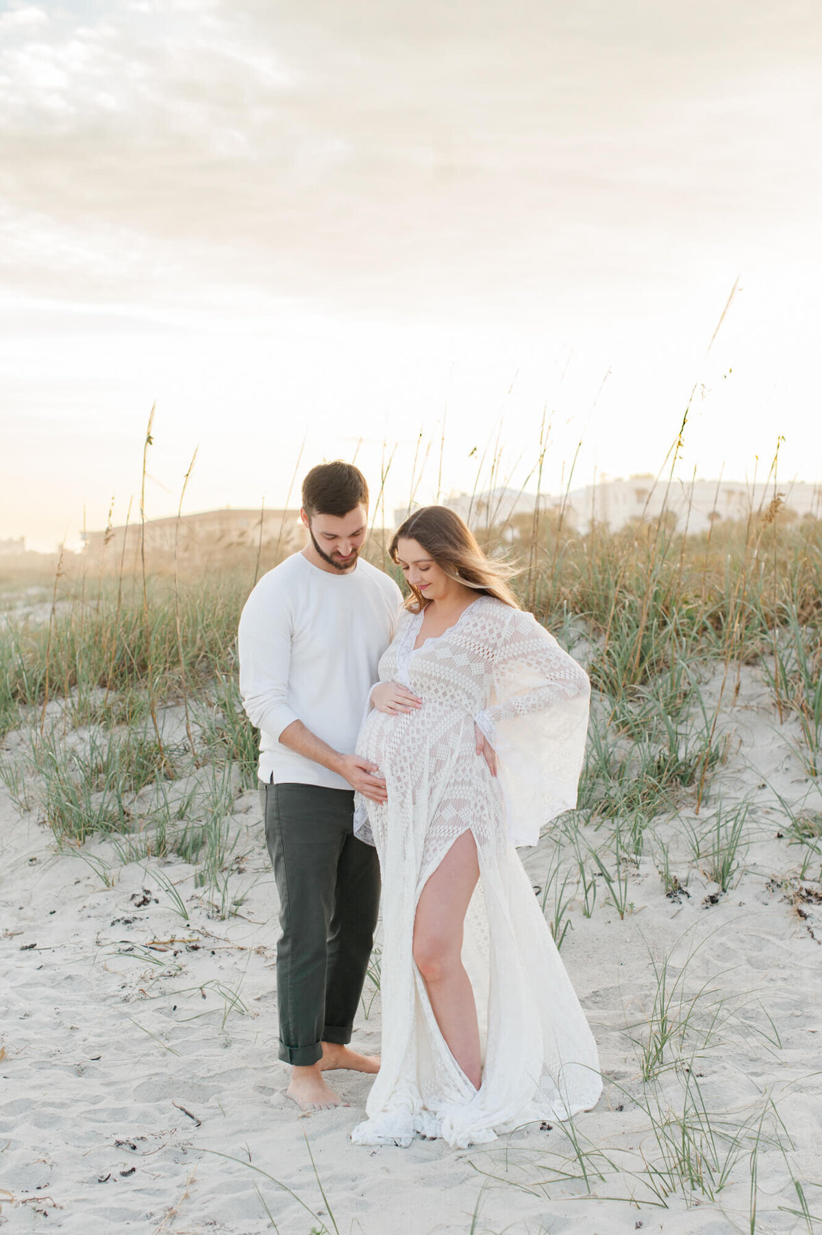 New parents stand in the dunes admiring moms belly and thikning of their new baby girl