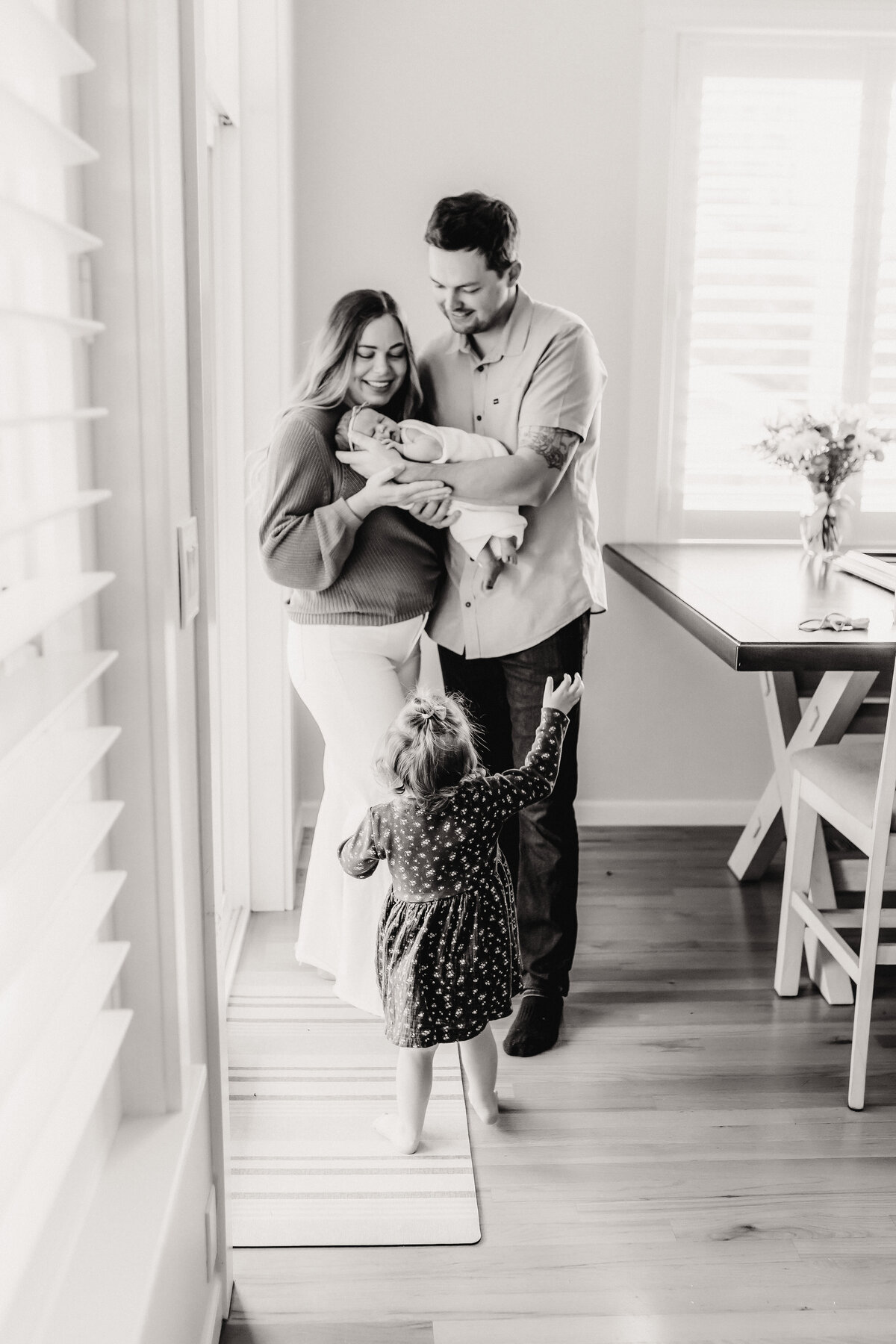 A young family stands inside their Vancouver Washington home holding and admiring their newborn baby