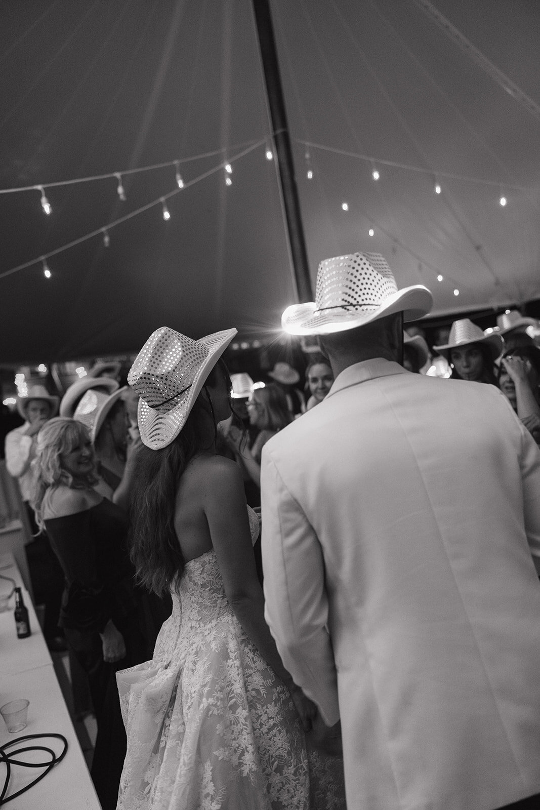 Black and white photo of bride and groom dancing under the tent wearing light-up cowboy hats at their Highlands, NC wedding reception.