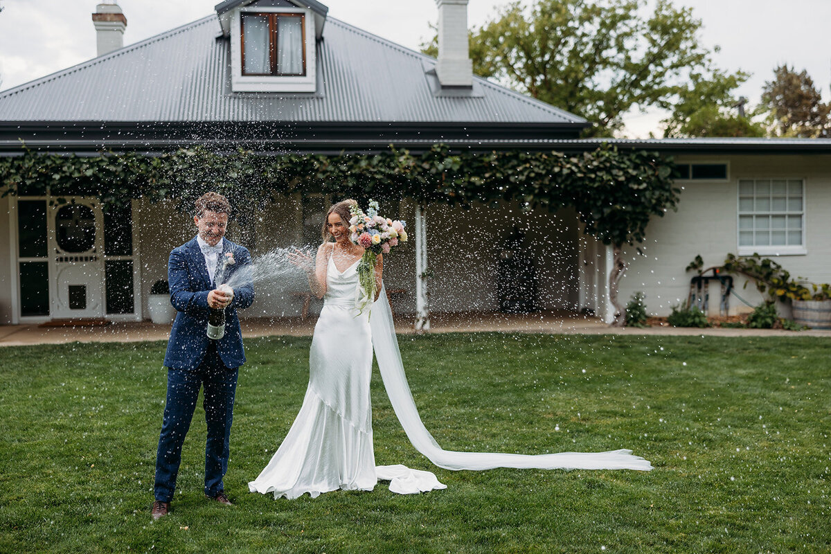 Groom spraying champagne with bride outside the homestead at Poachers Pantry