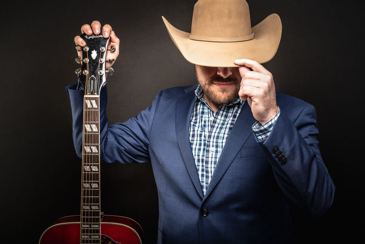 Personal branding portrait of a musician tipping his cowboy hat while holding a guitar.