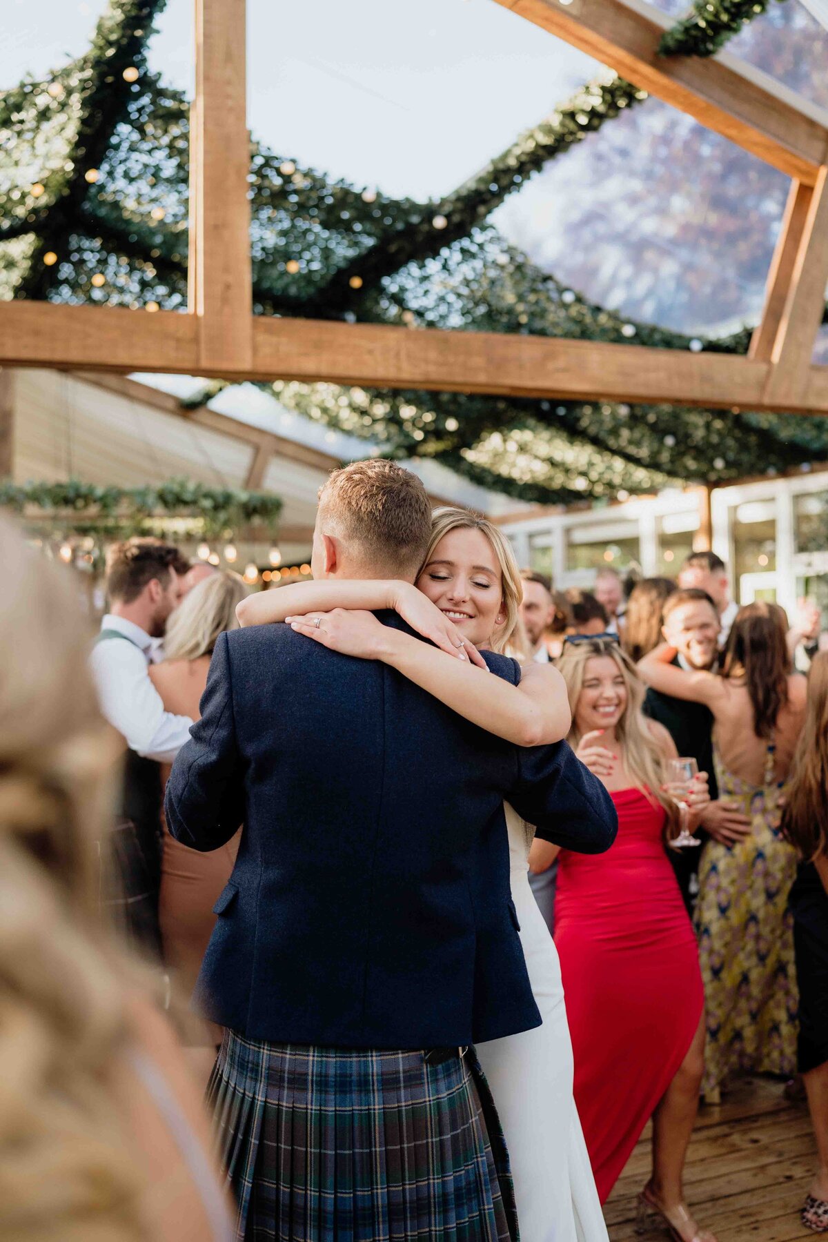 A couple embraces and dances at their wedding reception at House of Elrick wedding venue in Aberdeen. Guests in formal attire are photographed surrounding them, creating a joyful atmosphere.