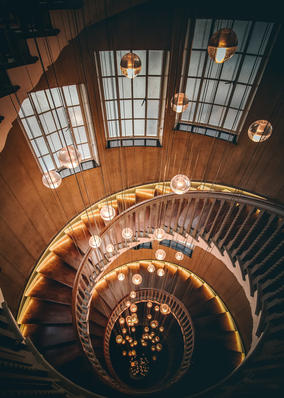 A spiral staircase twirls around a stunning lighting centrepiece as part of a luxury interior decor.