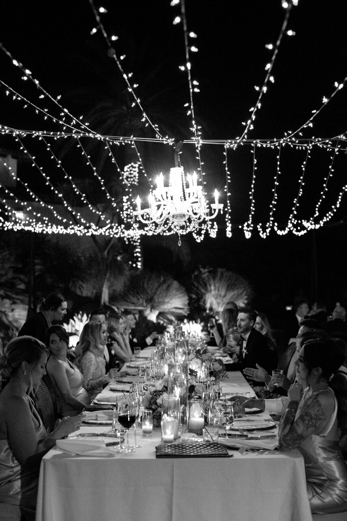 A reception table under string lights at nighttime with everyone engaging in conversation.