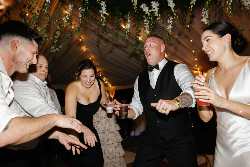 A lively and fun reception moment as the bride and groom dance with their guests under a beautifully decorated tent with twinkling lights and hanging florals. Captured by Claudia Amalia Photography, a Florida Keys wedding photographer specializing in destination wedding photography.