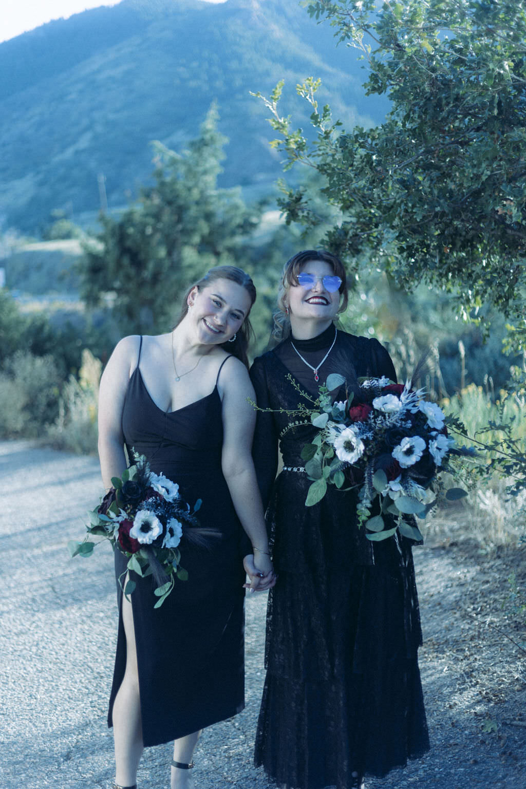 Two people in black dress holding hands and bouquets of flowers.