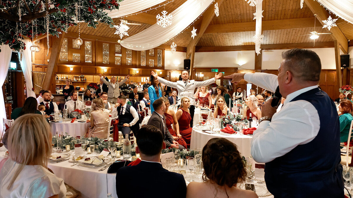 Father of the bride giving a fun lively speech with wedding guests having fun and standing at the wedding breakfast