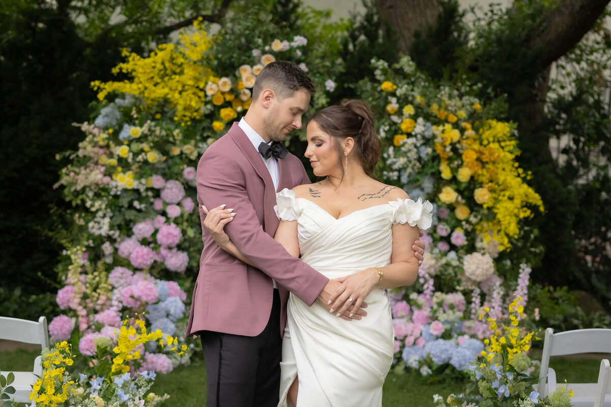 Bride and groom embracing in front of florals