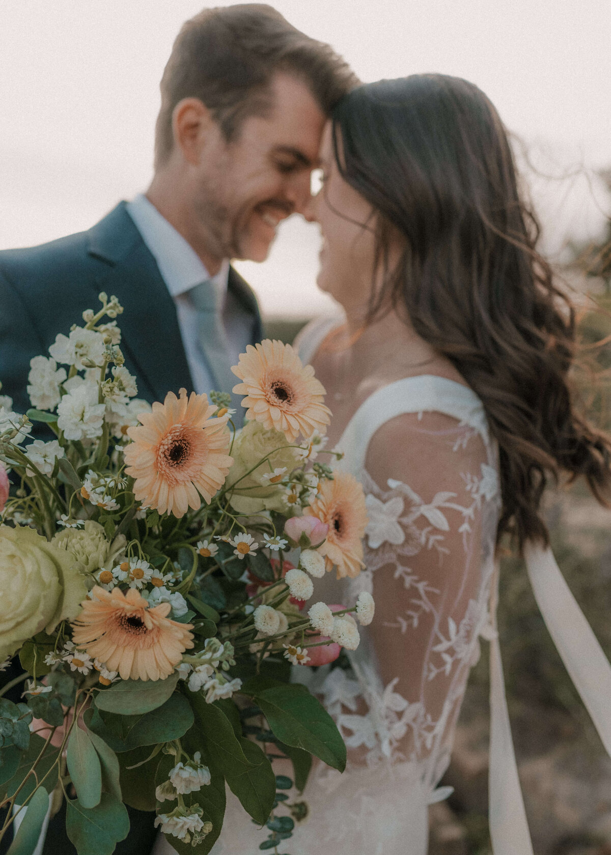 Bride holding colorful bouquet and smiling in close forehead to forehead to groom on Mogollon Rim in Payson, Arizona