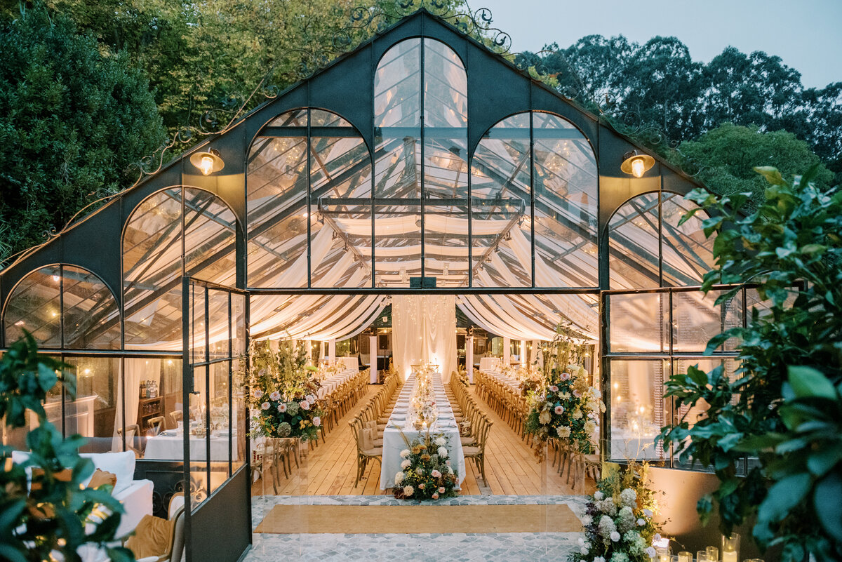 Greenhouse filled with white tables and florals for an intimate wedding reception dinner