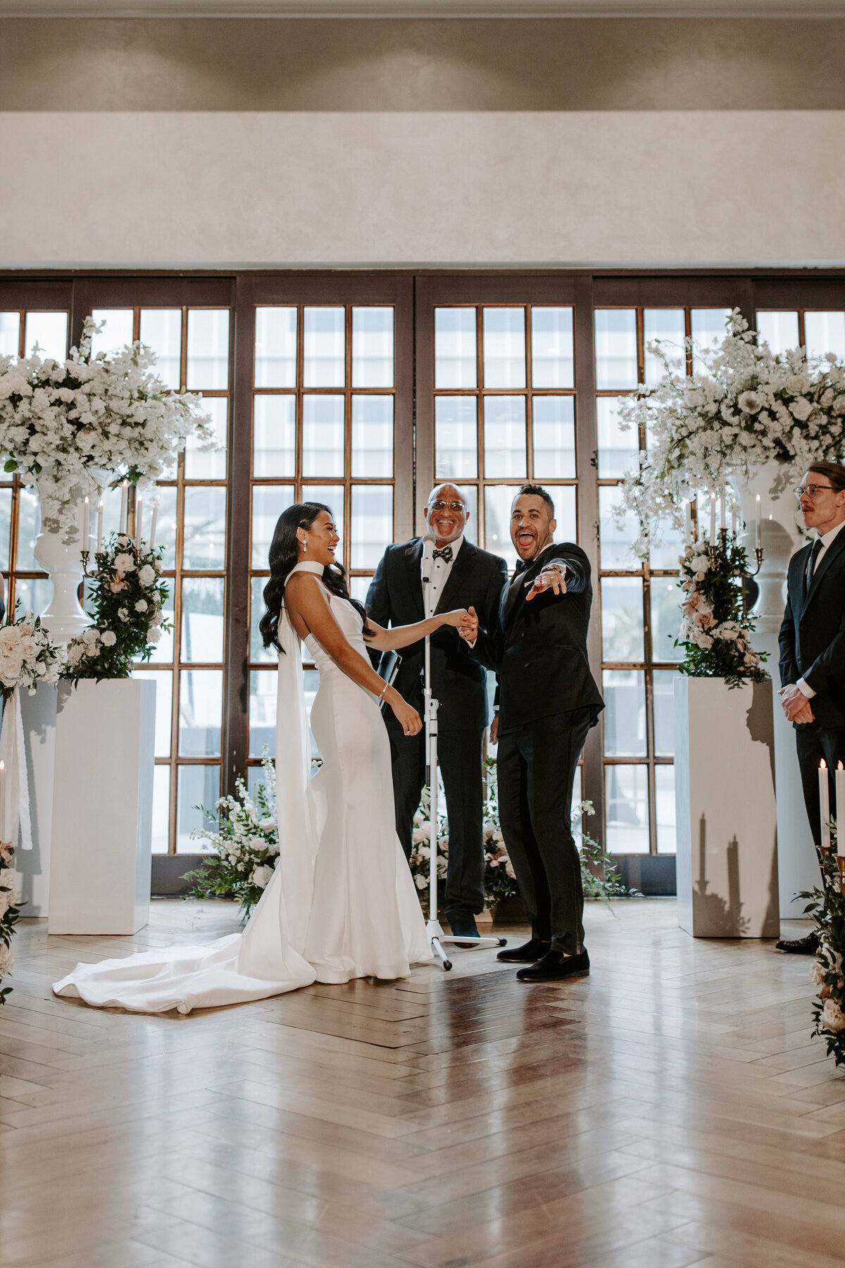 A groom holds hands with their partner while pointing at the audience during their ceremony at The Stirling Club.