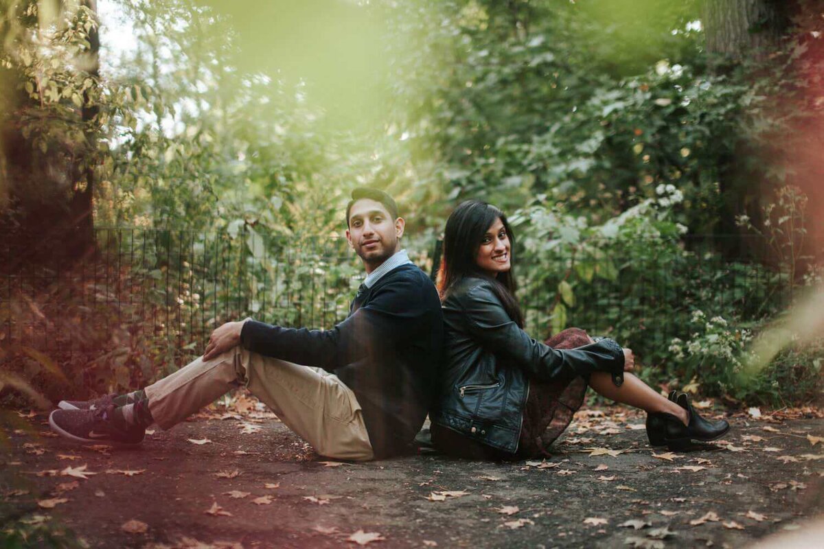 Couple sitting back to back in forest surrounded by greenery in Philadelphia.