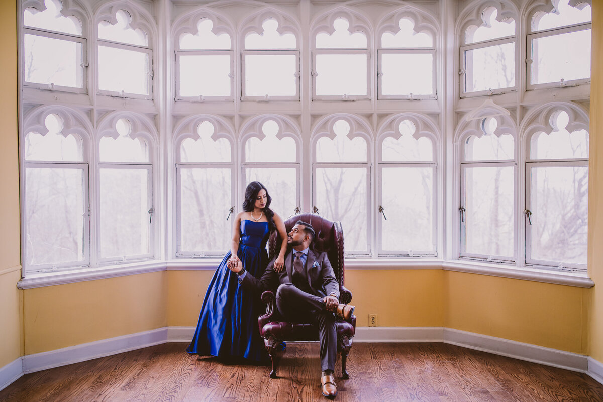 A classy couple sitting inside the hempstead house at sands point preserve in formal blue outfits