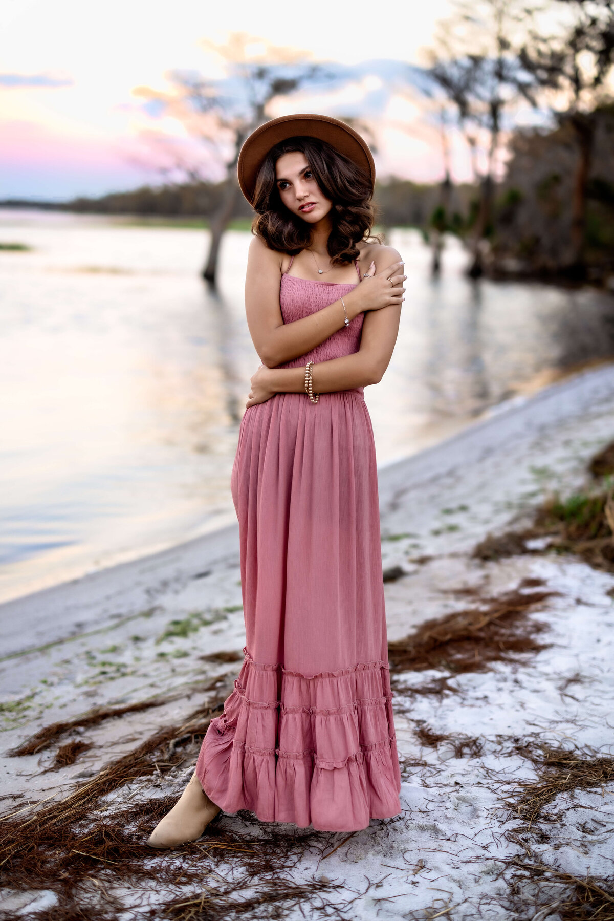 Bold senior girl in a very vogue like pose holding arms and standing on the shoreline of swampy lake in Winter Garden Florida
