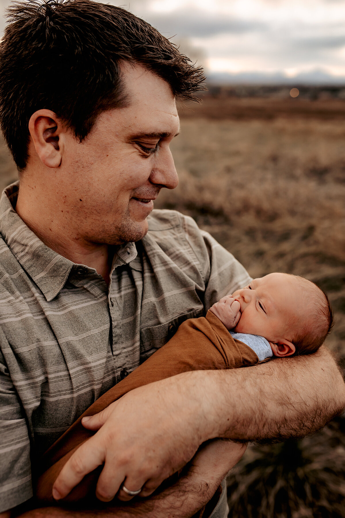 father holding newborn in front of mountains in denver