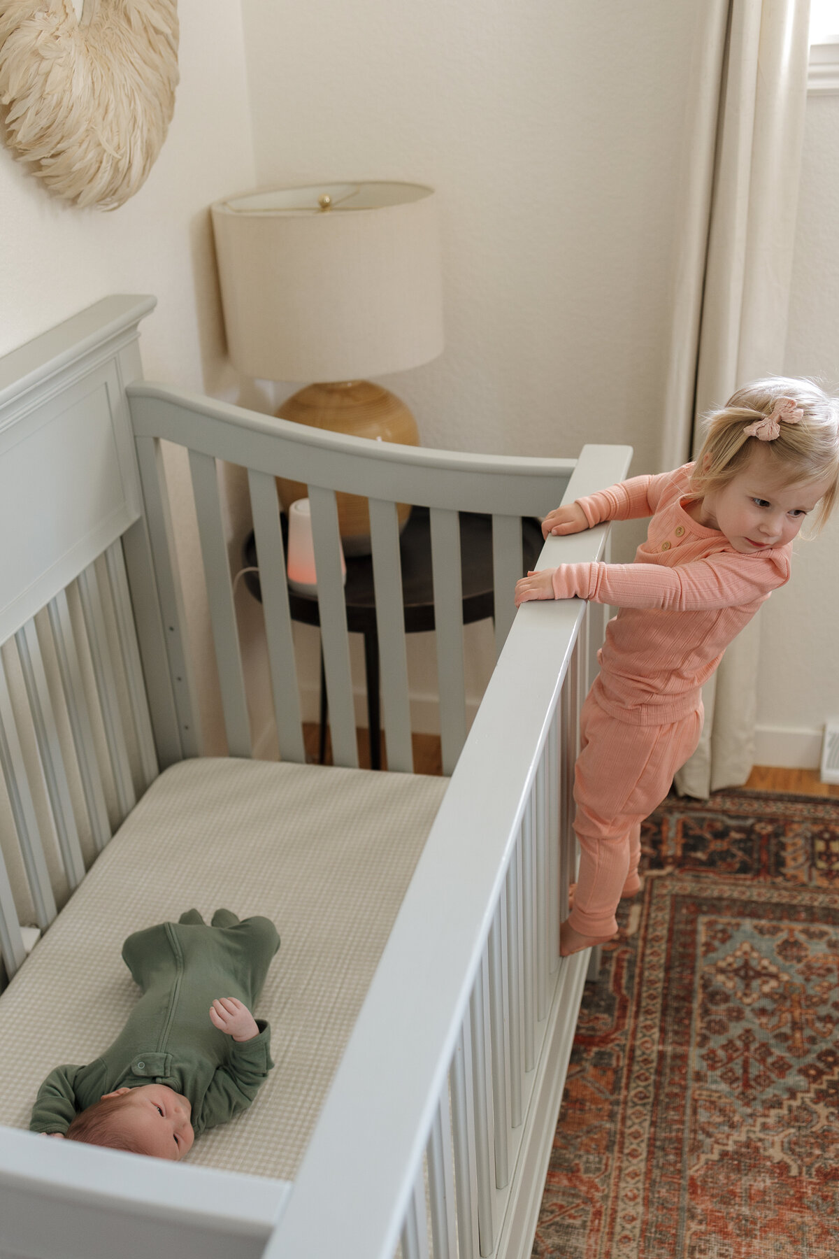 Longmont toddler climbing up on crib to look at newborn sibling