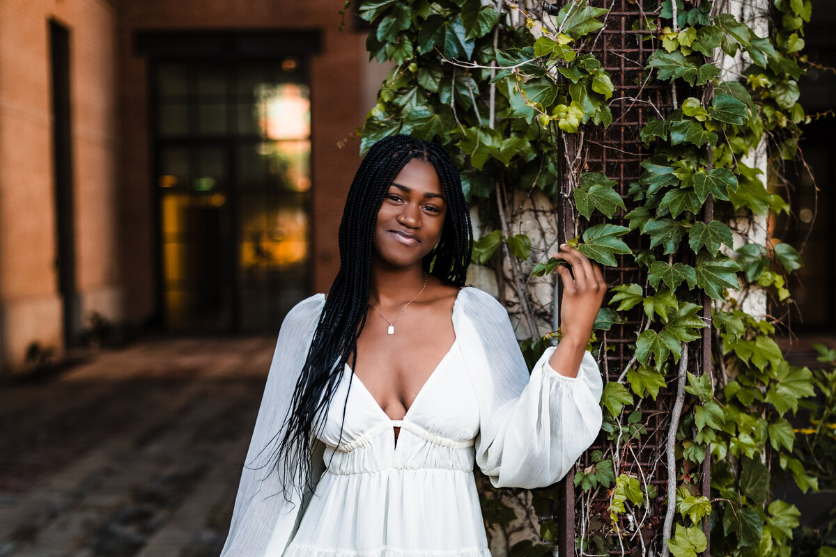 Senior girl posing in front of ivy-covered wall in white dress at The Pearl, soft and elegant vibe
