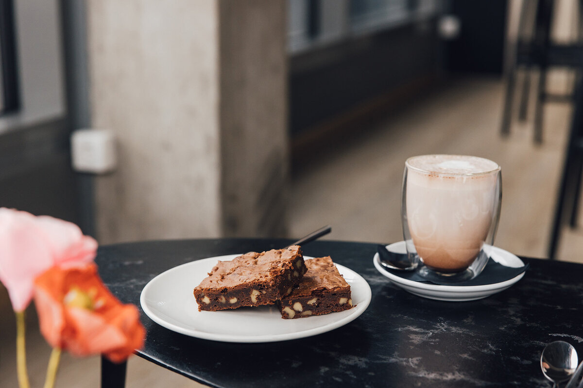 Zwei Stück Schokobrownies auf einem Teller und ein Glas mit heißer Schokolade
