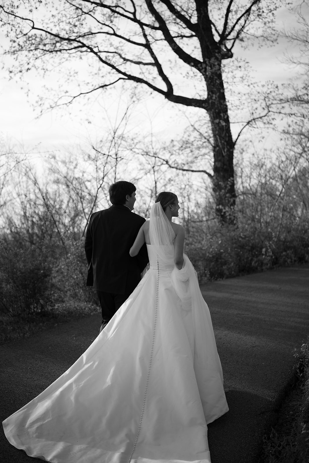 Black and white photo of the bride and groom walking together down a quiet path after their wedding ceremony at Burritt on the Mountain in Huntsville, Alabama, photographed by Perry Hancock.