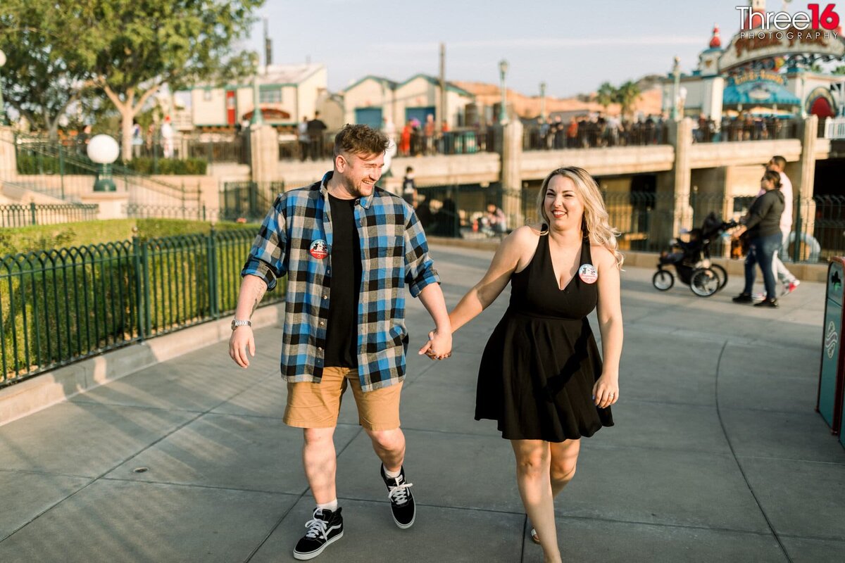 Engaged couple walk through Disneyland California Adventure holding hands during their engagement session.