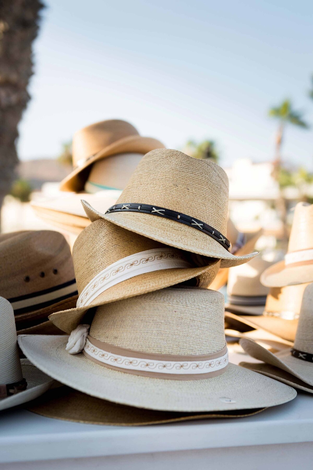 A stack of straw hats sits on a table as a welcome gift with tropical resort scene in the background.