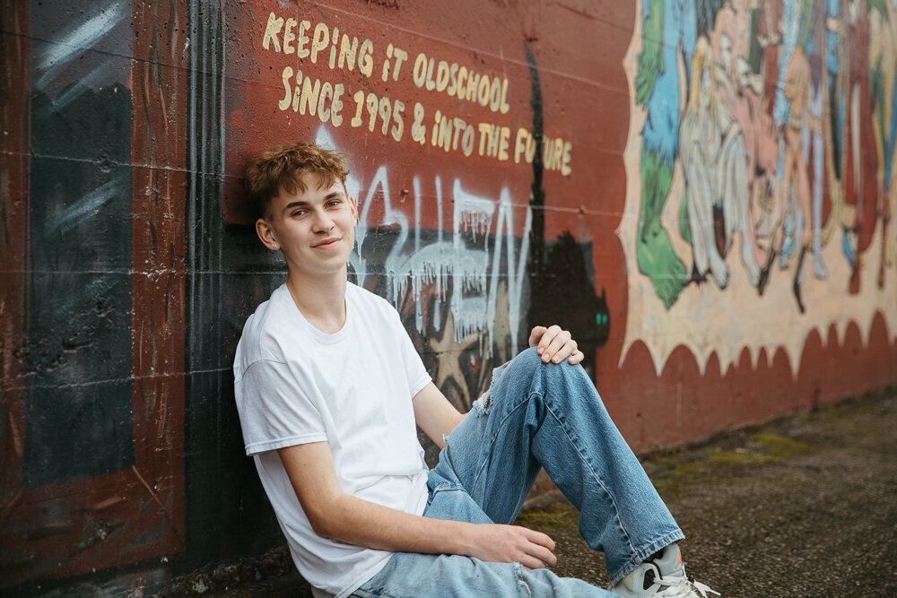 High school boy leaning against a graffiti wall in downtown Olympia WA