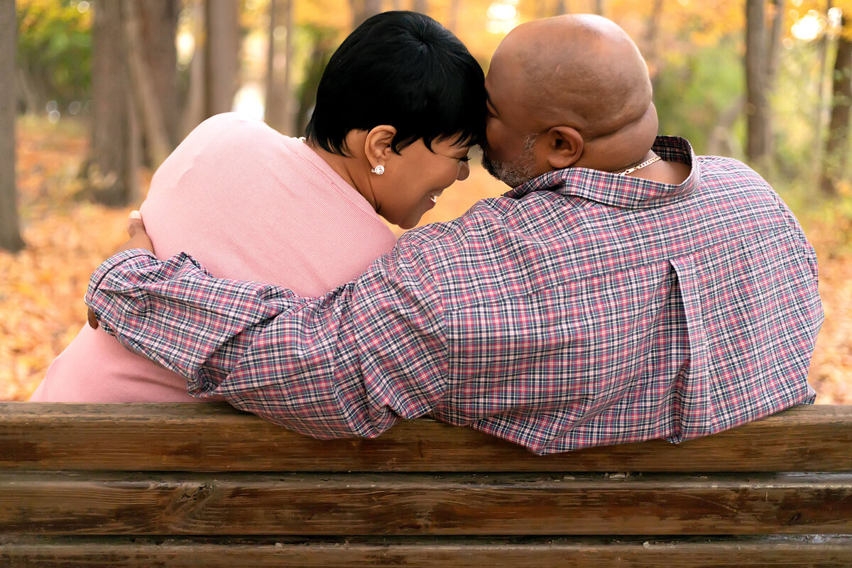 Couple sitting on bench while husband kisses the forehead of his wife