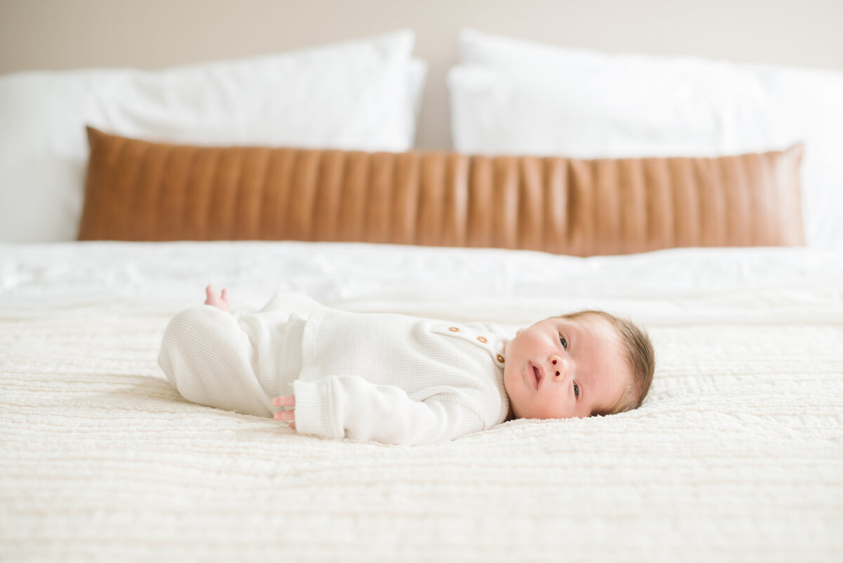 Baby in white onesie laying on bed - Washington DC Newborn Photographer