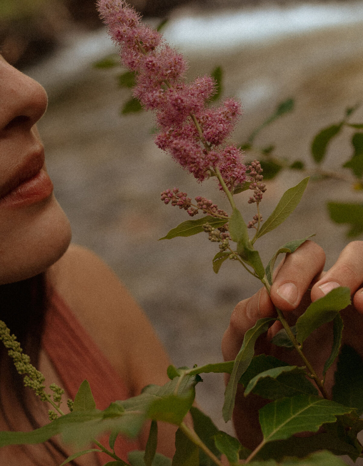 female entrepreneur smells pink flowers at river photoshoot in Bend, Oregon