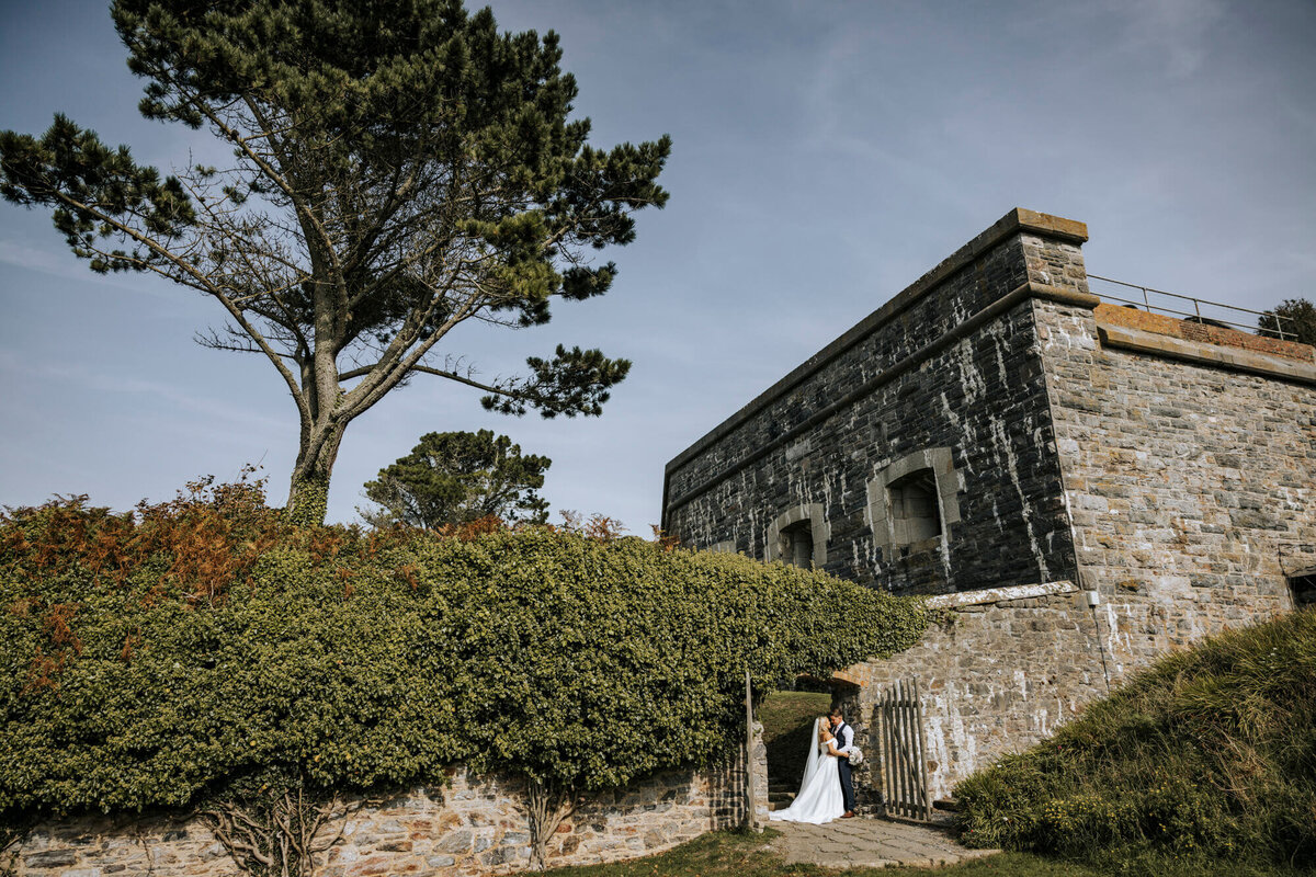 A bride and groom standing in front of Polhawn Fort