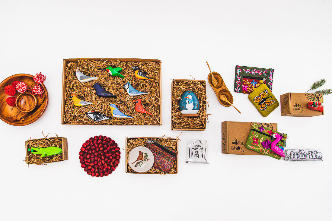 A flat lay arrangement of various decorative items displayed on a white background. The collection includes several small boxes filled with what looks like wood shavings containing ornaments, some decorative birds, small gift items, and what appears to be cranberries or red berries.
