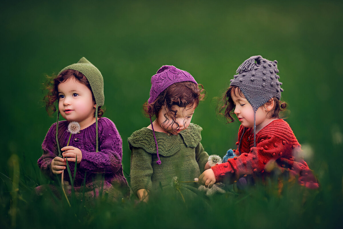 Three young sisters sit in a meadow wearing crocheted garments in an enchanted photo session with Kara Reese.