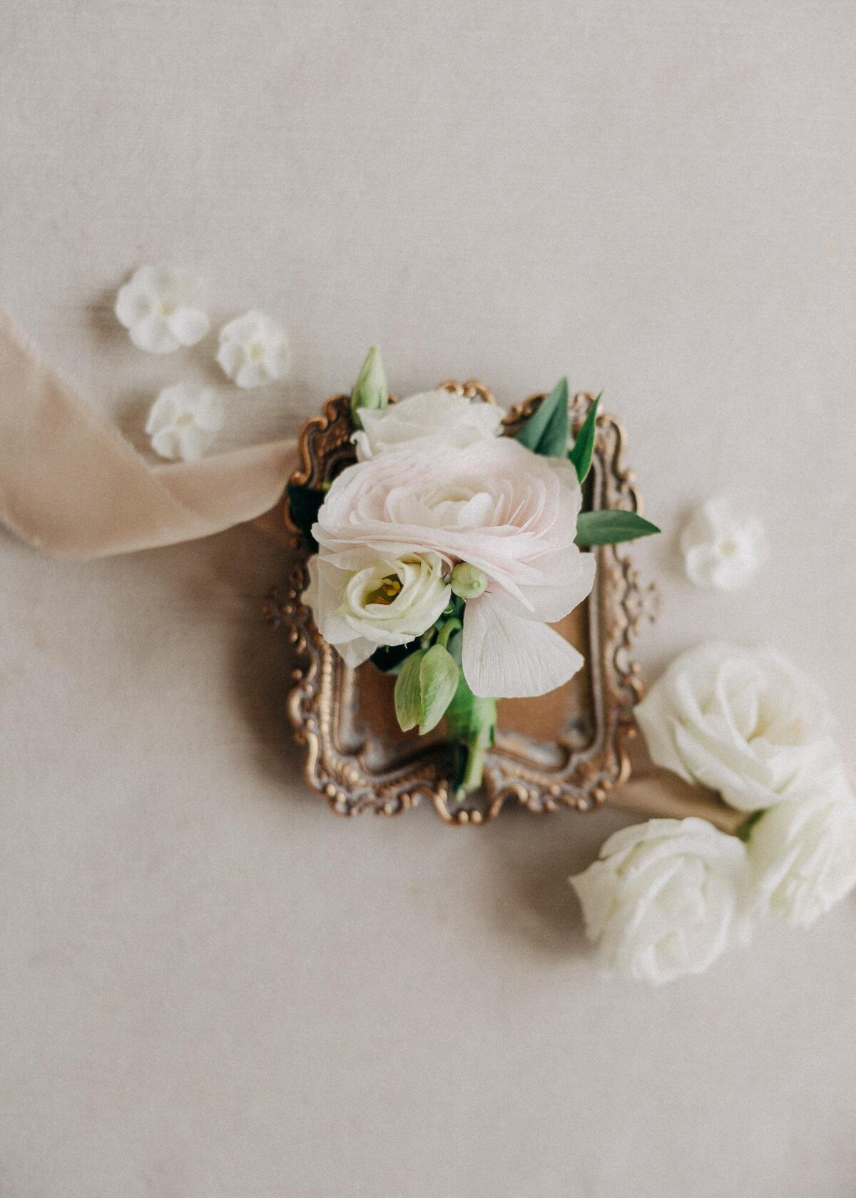 An elegant floral arrangement on an antique frame, accompanied by delicate white flowers and a ribbon on a neutral backdrop.