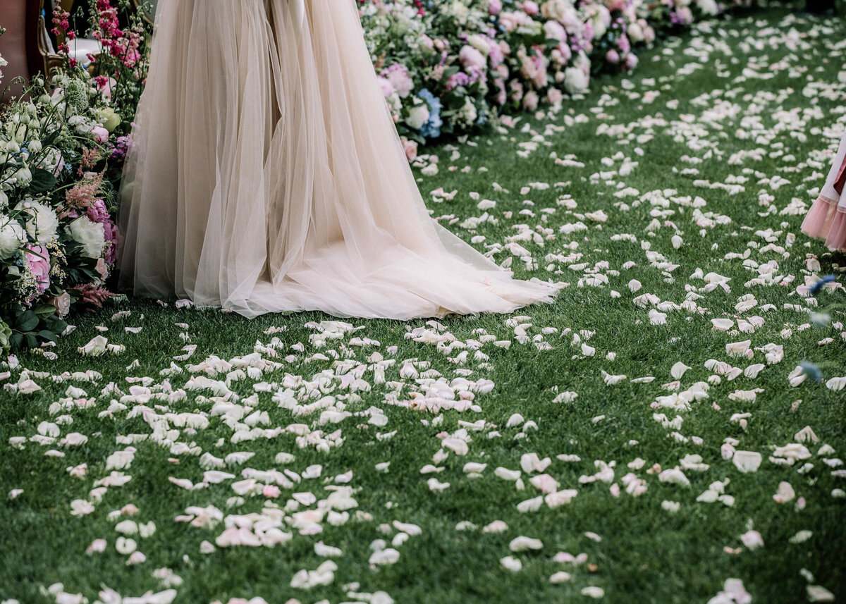 Rose petal confetti lies on the grass aisle lined with colourful flowers, and a luxury wedding dress.