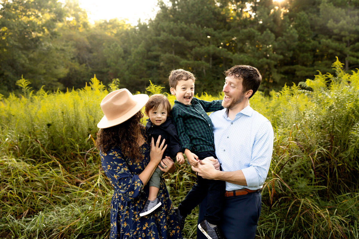 Parents holding young sons and laughing while standing in field during sunrise
