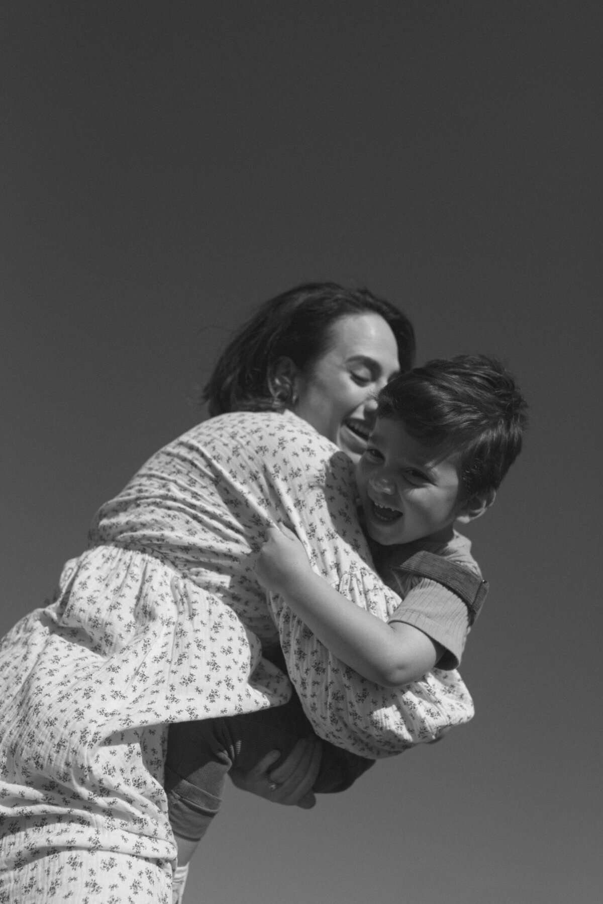a black and white photo of a mother holding her son smiling at him.