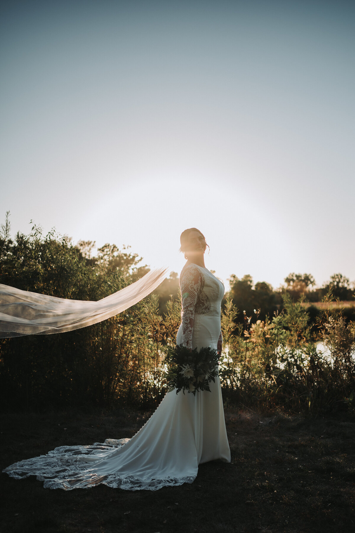 Bride standing with her beautiful dress backlit by the sun.