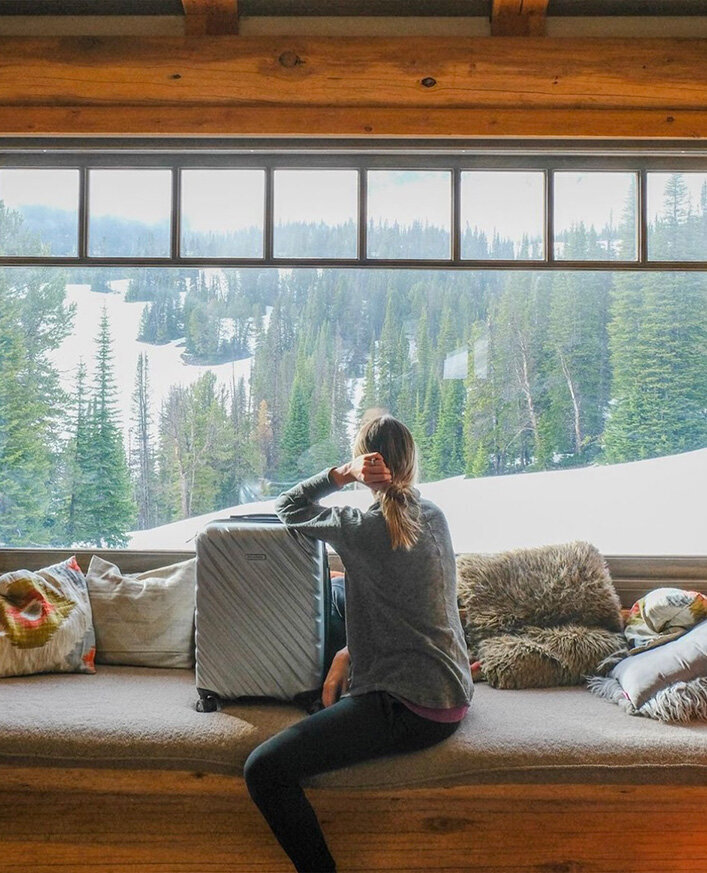 A woman sits on a window sill with a Ricardo brand suitcase, looking thoughtful, representing the theme of travel and new beginnings.