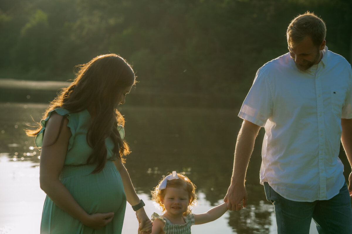 maternity photos of a husband and wife and child walking near the shore of lake degray near caddo valley, arkansas